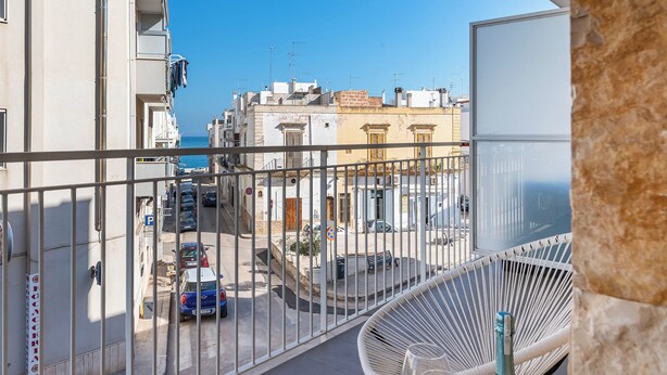 Un balcón con vista a una calle, una silla y una botella de vino.