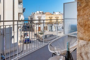 Un balcon donnant sur une rue, une chaise et une bouteille de vin.