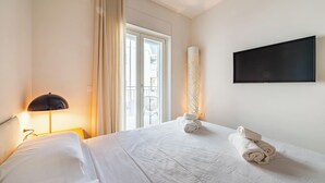Una habitación de hotel con una cama, un televisor montado en la pared y una ventana con cortinas.
