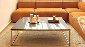 Un salon avec un canapé d’angle, une table basse en verre et un luminaire suspendu.