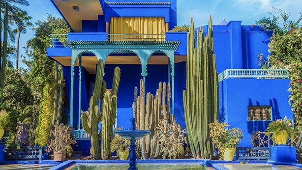 Un bâtiment bleu avec une fontaine et des cactus au premier plan.