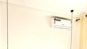 Un lit bien fait, avec du linge de lit blanc et des oreillers, une table de chevet avec une lampe et un climatiseur fixé au mur.