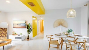 A modern dining area with a white table set for four, surrounded by wicker chairs. - 2BR Hollywood Broadwalk Haven | Free Parking (Hollywood)