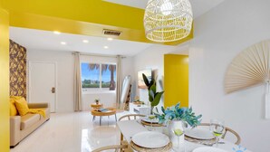 A dining area with a white table set for four, surrounded by yellow walls and a large woven light fixture. - 2BR Hollywood Broadwalk Haven | Free Parking (Hollywood)