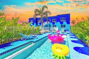 Une piscine avec des jeux gonflables, une clôture blanche et un bâtiment aux murs bleus.