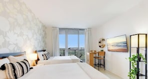 Quarto de hotel com duas camas, uma mesa, uma cadeira, televisão, varanda com vista e uma planta.