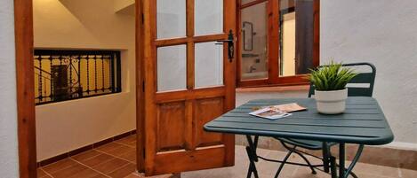 Una puerta de madera con paneles de vidrio, una mesita con una planta en maceta y una silla.