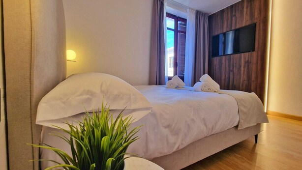 Ein modernes Hotelzimmer mit einem Bett, einer Zimmerpflanze, einem an der Wand montierten Flachbildfernseher und einem Fenster mit Vorhängen.