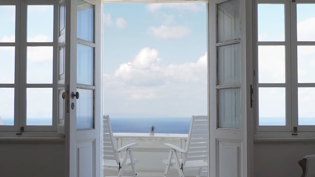 An open door leading to a balcony with two white chairs and a table, overlooking a scenic ocean view. - The Palm Rock Finikia Santorini (Santorini)