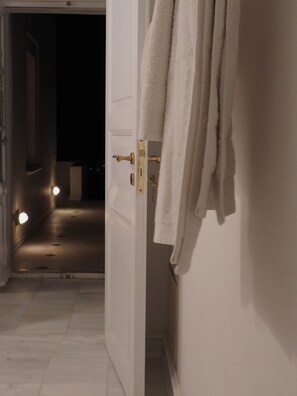 An interior hallway with a white door leading to a dark room. There are white towels hanging on the wall and a brass door handle. - The Palm Rock Finikia Santorini (Santorini)