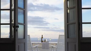 An open door with a view of a balcony table set with two white chairs, a bottle, and a glass. - The Palm Rock Finikia Santorini (Santorini)