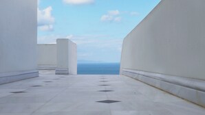 A corridor with white walls and a tiled floor leading to a view of the sea. - The Palm Rock Finikia Santorini (Santorini)