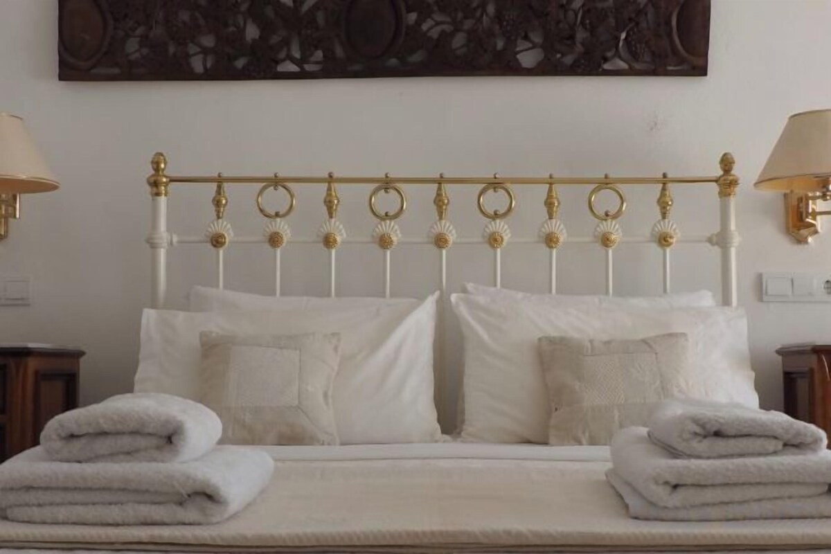 A bed with a gold headboard, white bedding, and two bedside lamps.