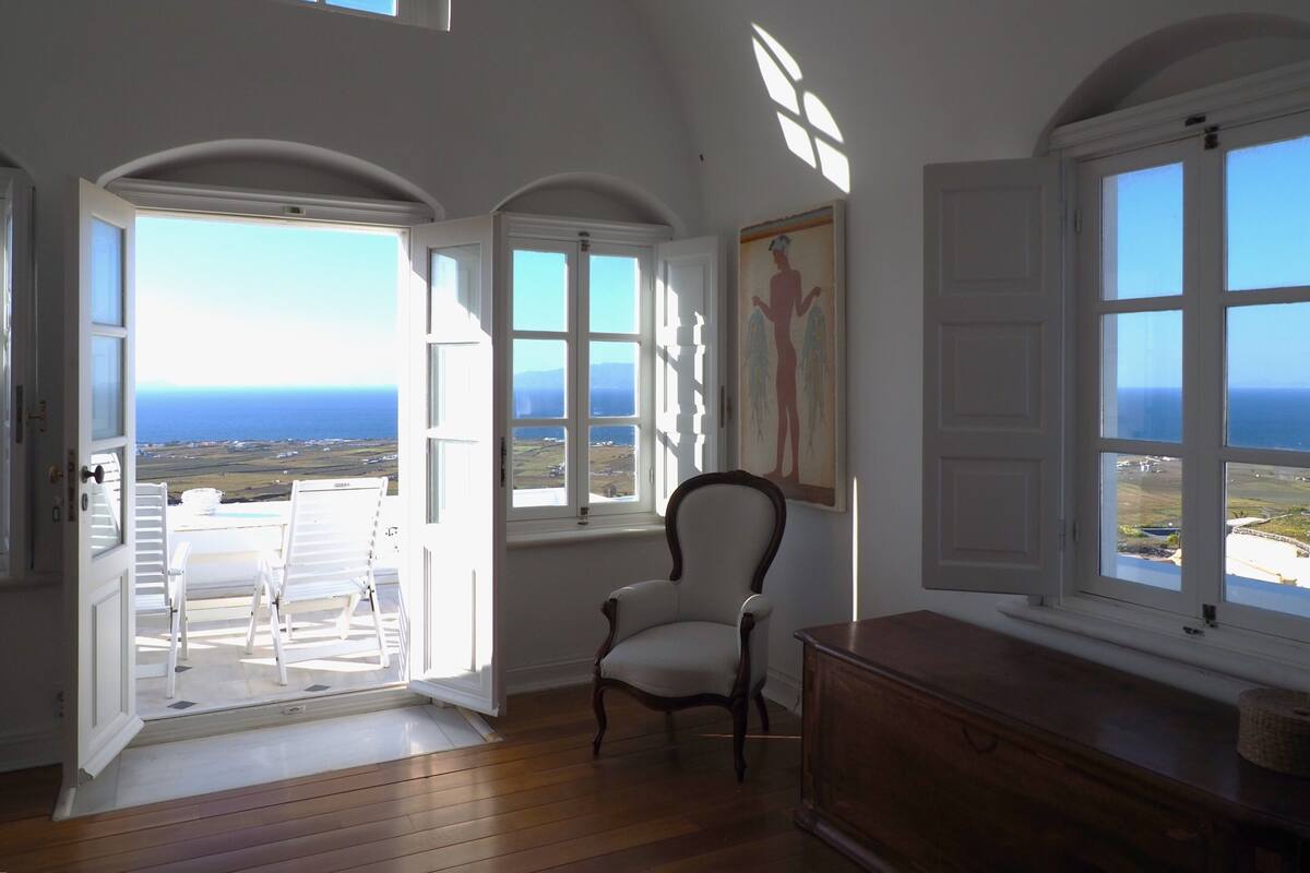 A room with a view of the ocean, a chair, and a wooden dresser.
