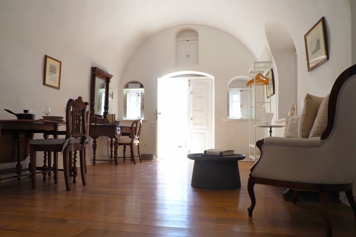 A spacious living room with wooden flooring, a dining area with a table and chairs, and a cozy seating area with a sofa.