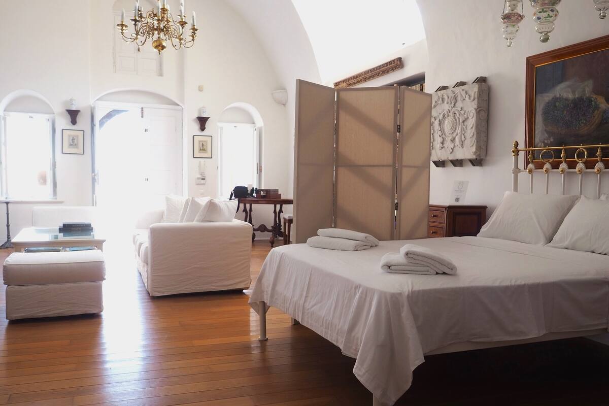 A spacious bedroom with a large bed, a sitting area with a sofa, and a dining table.