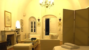 A hotel room with a bed, a sofa, a table, a fireplace, and a door. - The Palm Rock Finikia Santorini (Santorini)