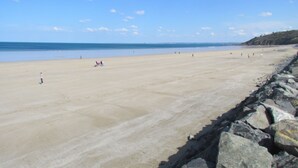 Una extensa playa de arena con costa rocosa y cielo azul despejado.