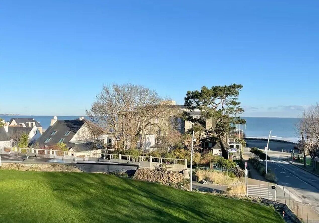 Ein Küstenwohngebiet mit Häusern, einer grünen Vordergrundfläche und freiem Blick auf das Meer.