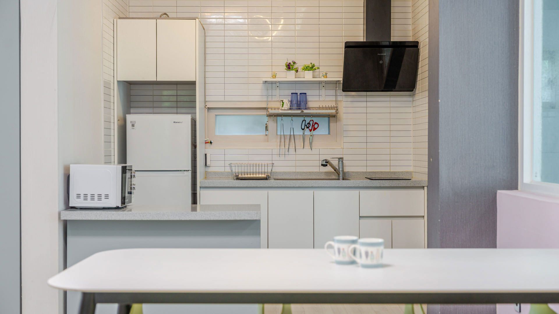 Una cocina moderna con armarios blancos, microondas integrado, refrigerador y campana extractora negra.