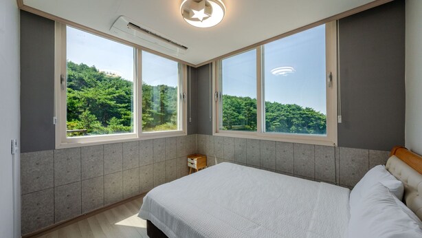 A bedroom with a large bed, two windows, and a view of greenery. - Taean Blueisland Pool Villa (Taean)