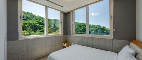 Un dormitorio con una cama grande, dos ventanas y vistas a zonas verdes.