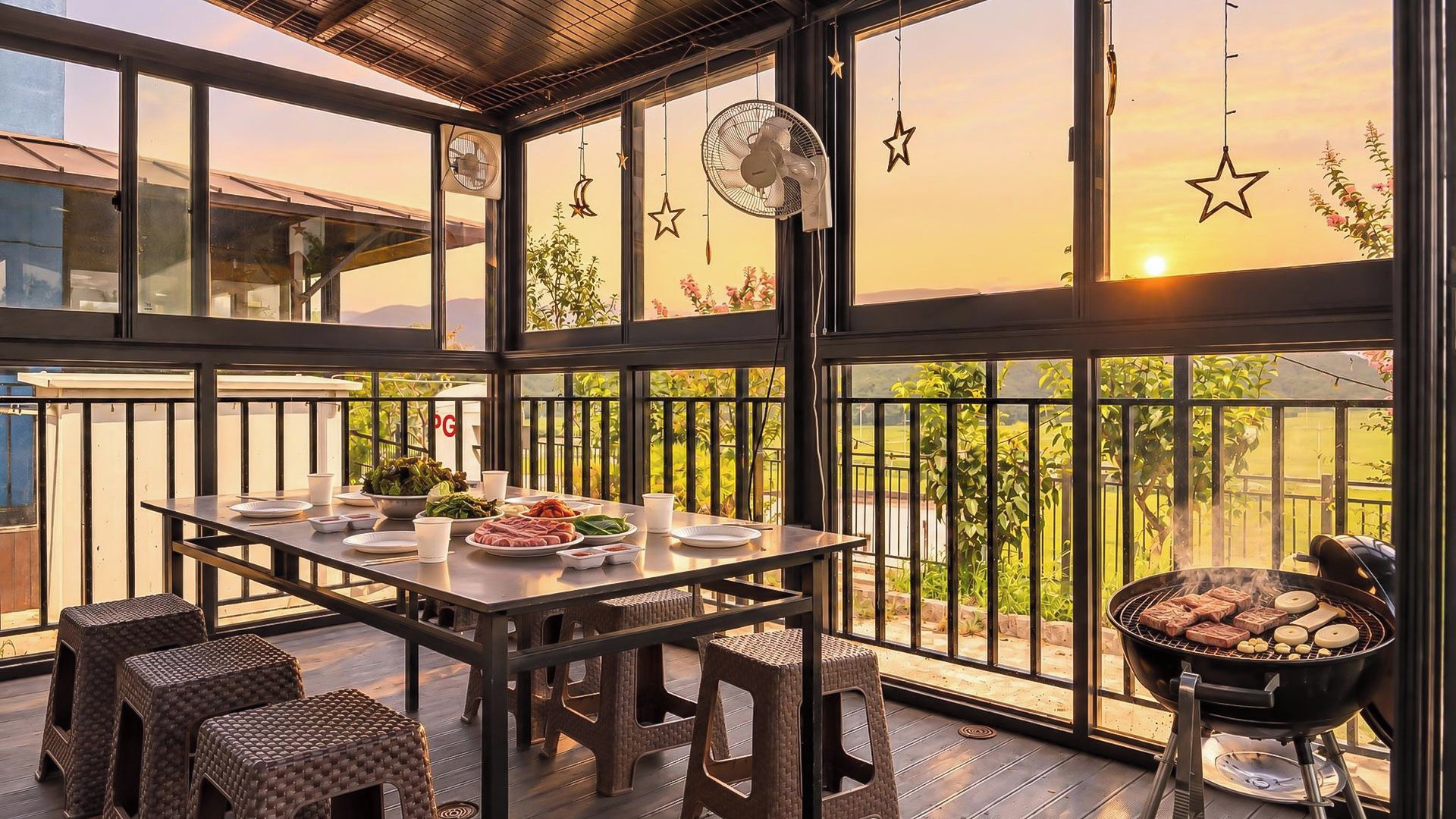 Een overdekt buiten eetgedeelte met een tafel gedekt voor een maaltijd, een barbecue en uitzicht op de zonsondergang.
