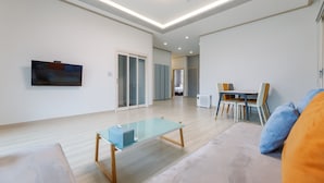 Una sala de estar moderna con una mesa de centro de vidrio, un sofá y una zona de comedor con sillas.