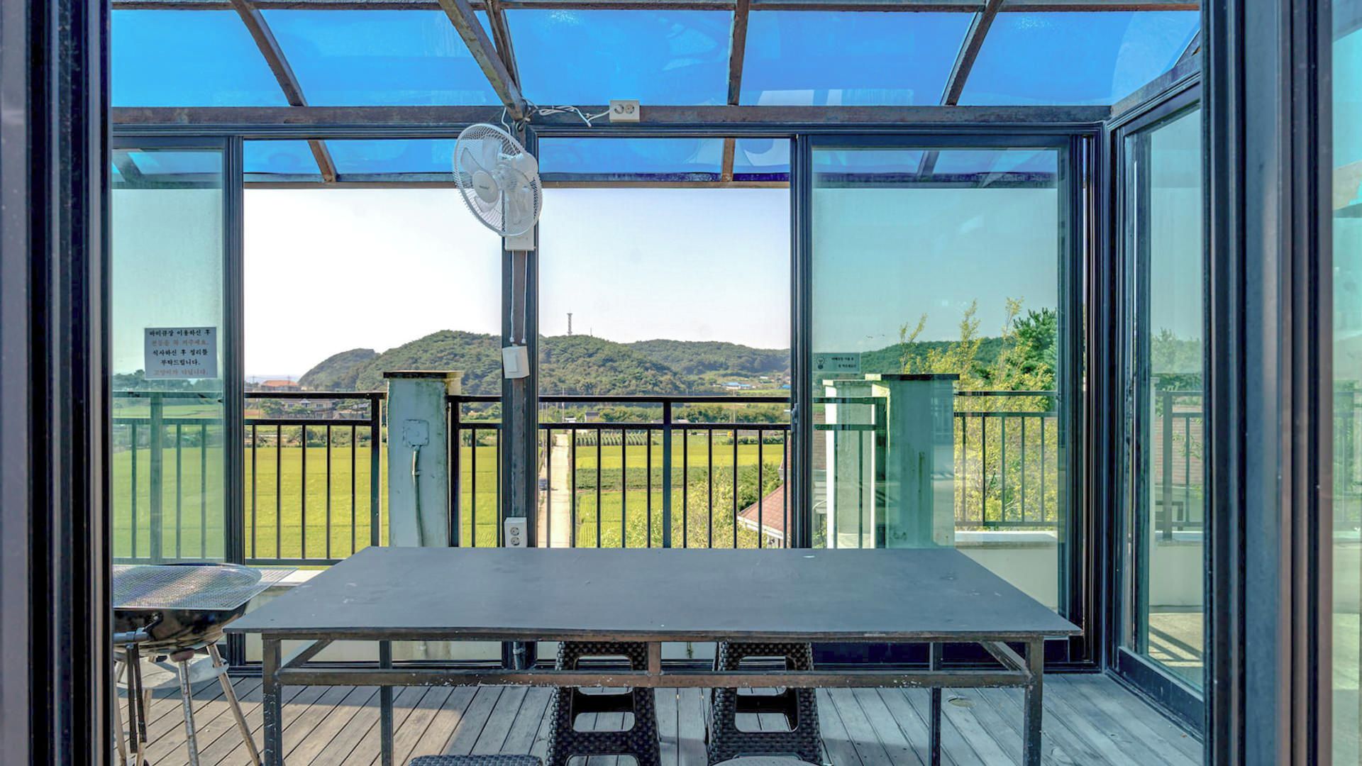 Un balcón con mesa y sillas, un ventilador y vistas a un paisaje verde con colinas.