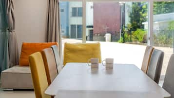 Un interior moderno con una mesa de comedor, sillas y un sofá con cojines. Dos tazas blancas están sobre la mesa.
