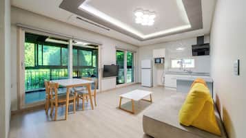 Una sala de estar moderna con comedor, un sofá con un cojín amarillo, un televisor y una cocina con microondas.