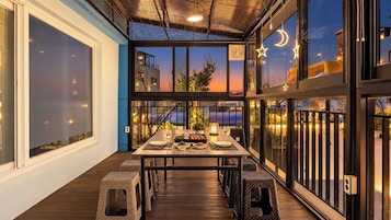Un área de comedor al aire libre con una mesa dispuesta para dos personas, rodeada de sillas de mimbre, con vista a un atardecer.