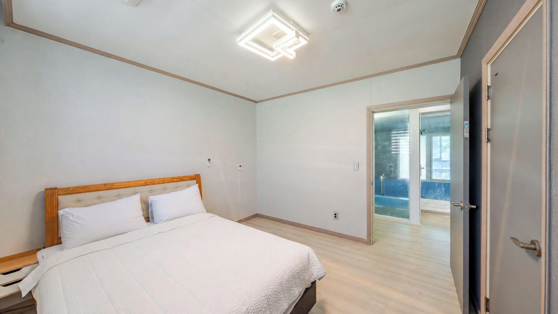 Une chambre à coucher avec un lit, un luminaire au plafond et une porte donnant sur une autre pièce.