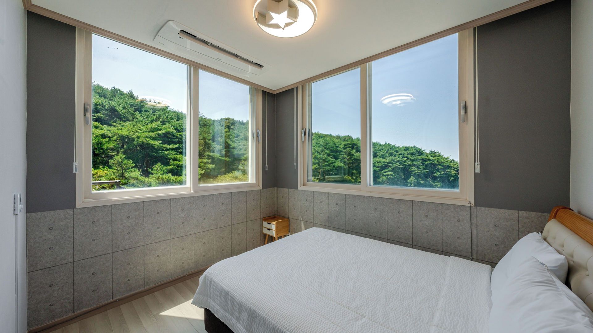 A bedroom with a large bed, two windows, and a view of greenery.