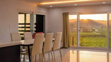 Un comedor moderno con una mesa y sillas, una zona de cocina con armarios, y un gran ventanal corredera que da a un balcón con vistas al paisaje.