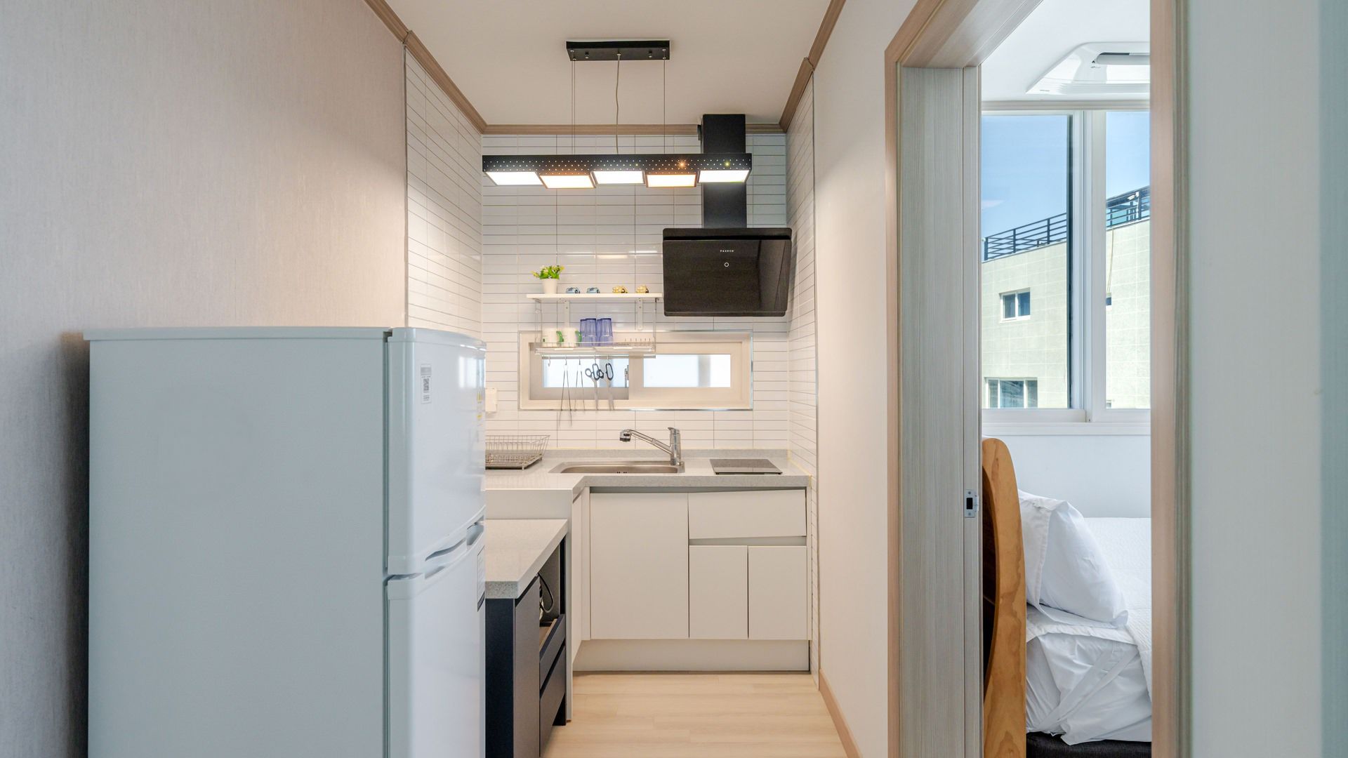 Una cocina compacta con horno integrado, un lavamanos y un ventanal que proporciona luz natural.