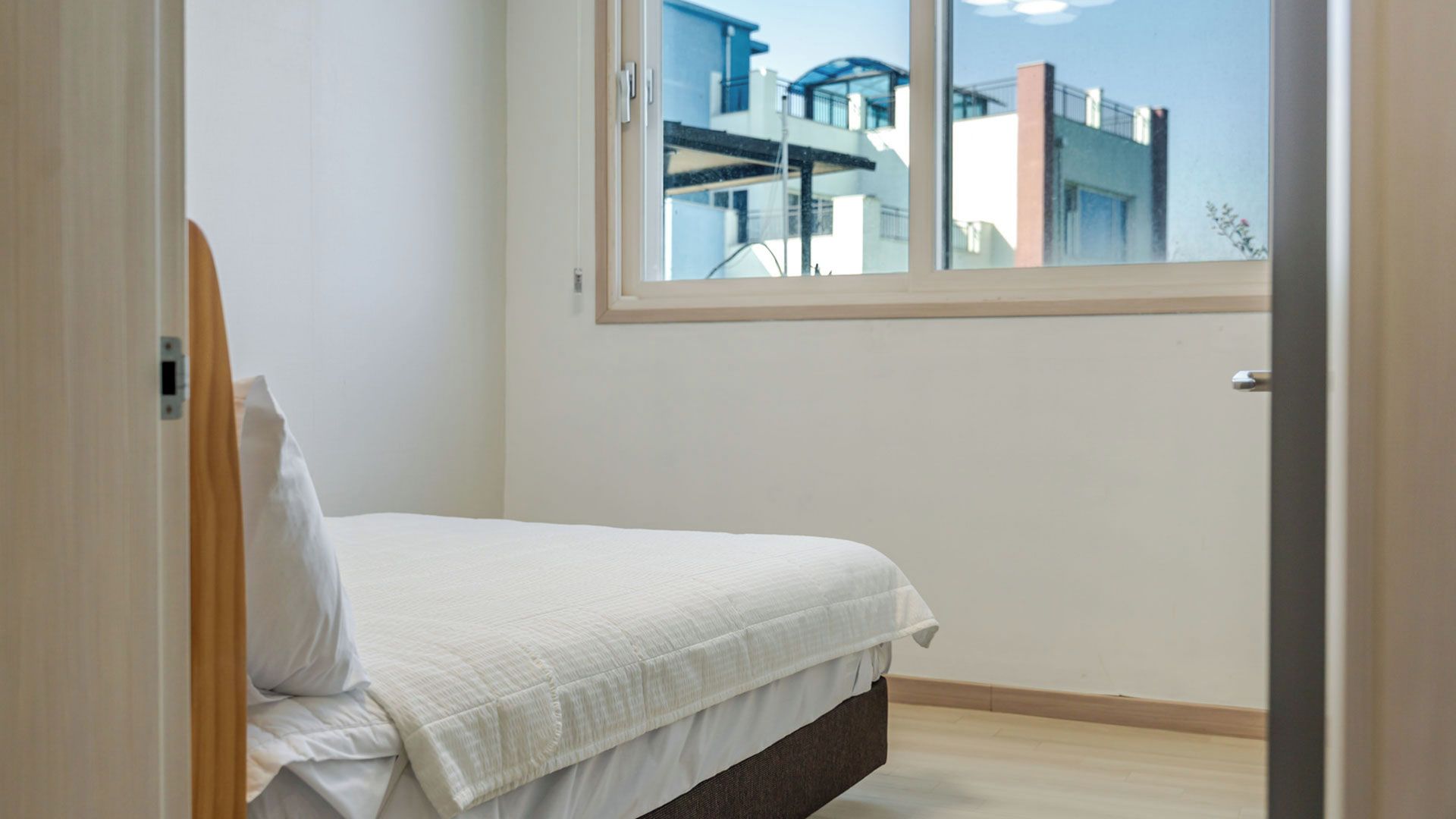 Un dormitorio con cama, ventana y vistas a edificios.