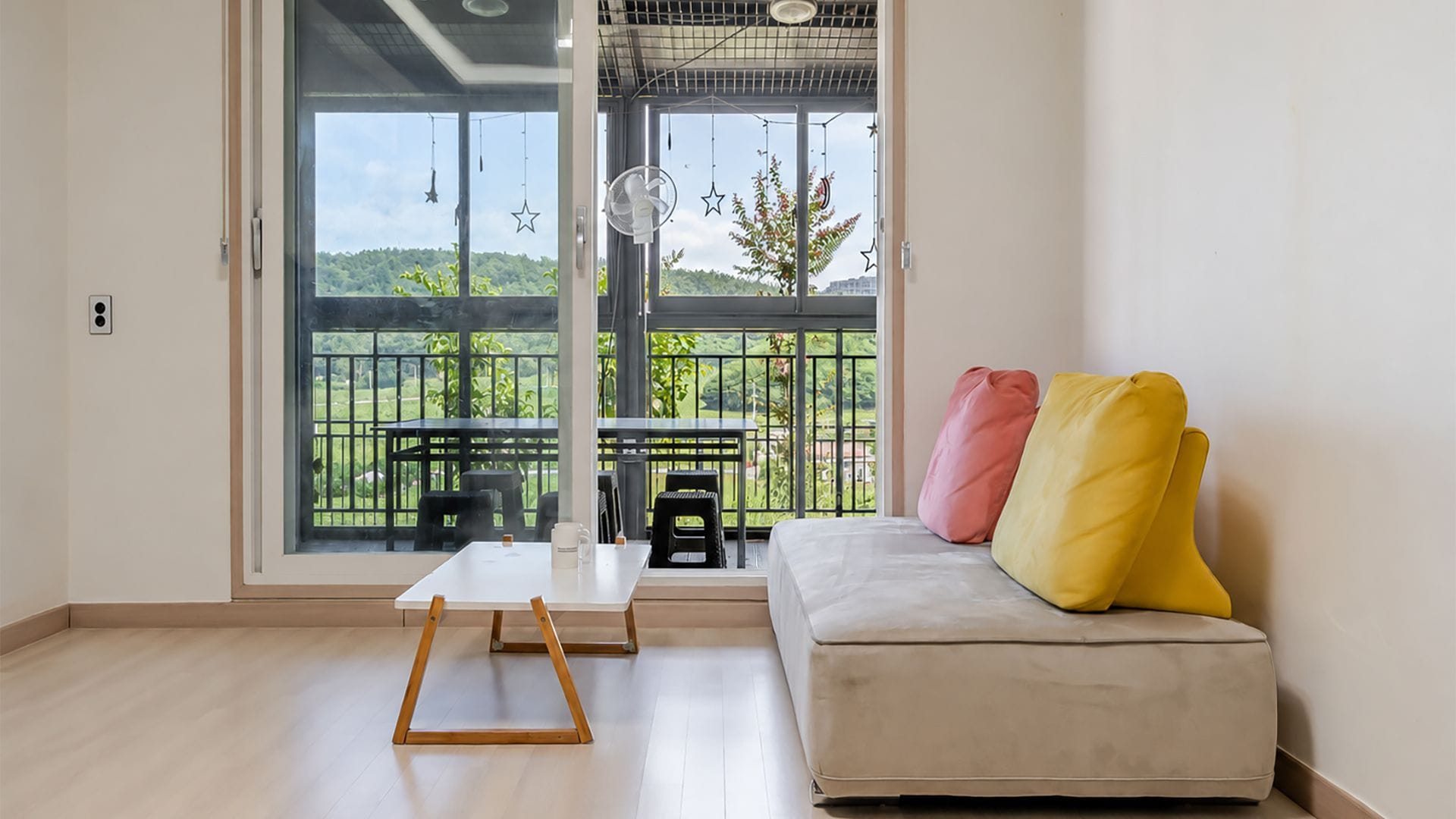 A room with a sofa, a small table, and a view of a balcony with outdoor furniture.
