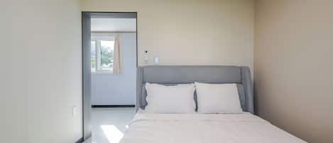 A bedroom with a bed, a door leading to a balcony, and a light switch on the wall.