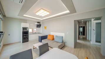 A modern hotel room with a kitchenette, a sofa with cushions, a dining table, and a separate bedroom area.