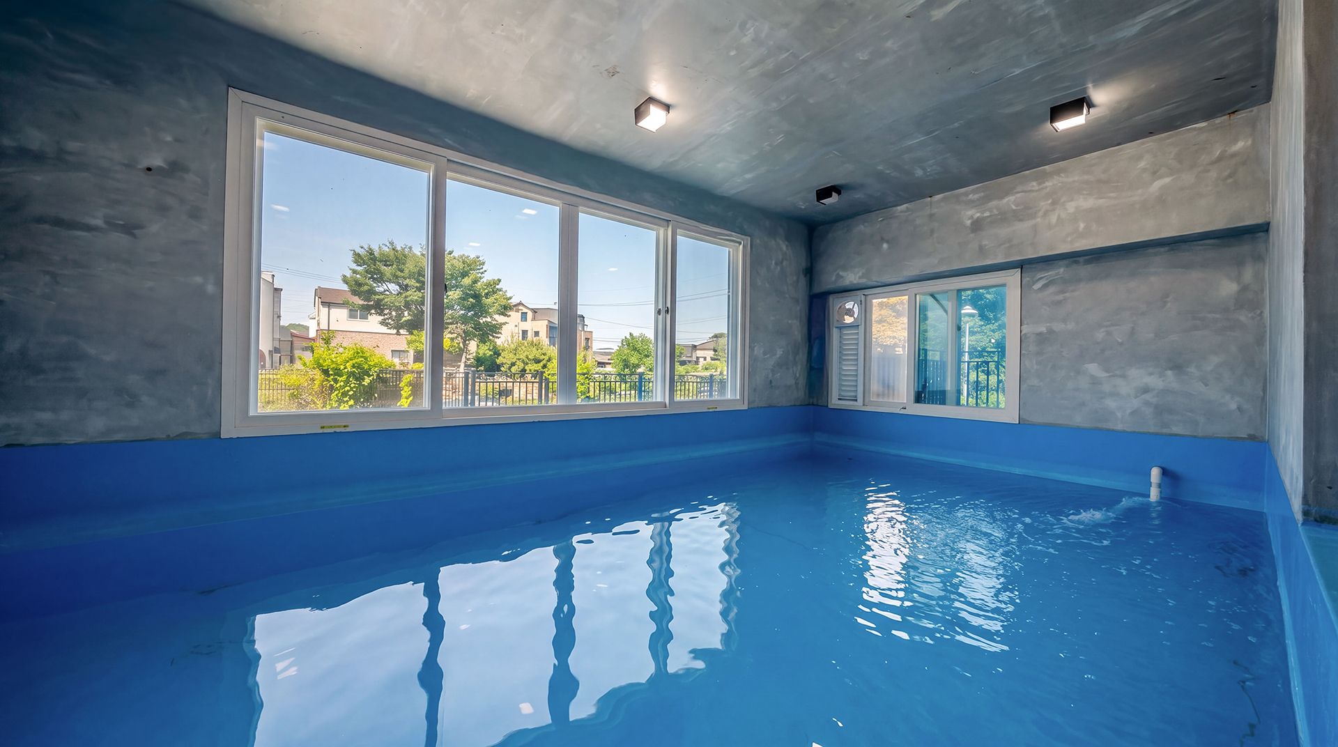 An indoor swimming pool with large windows and a view of the neighborhood.