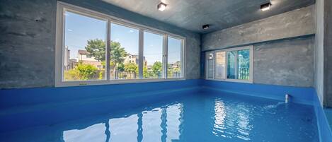 An indoor swimming pool with large windows and a view of the neighborhood.