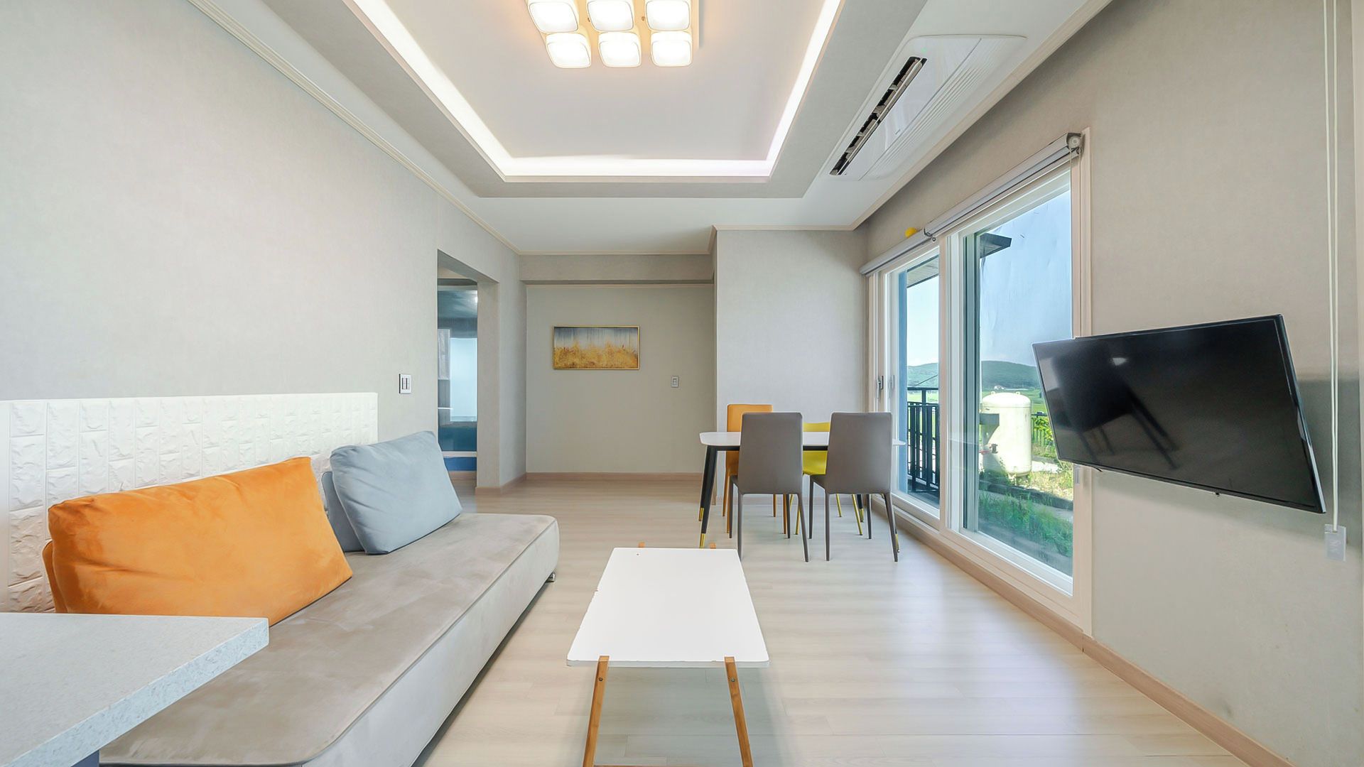 Uma sala de estar moderna com sofá, televisão de tela plana na parede e área de jantar com cadeiras e mesa.