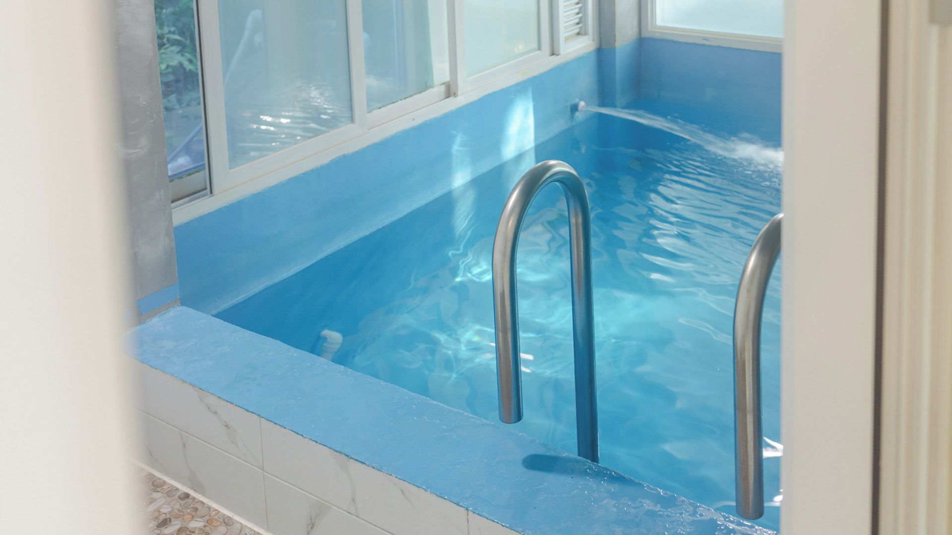 A swimming pool with a blue interior, clear water, and metal pool ladders.