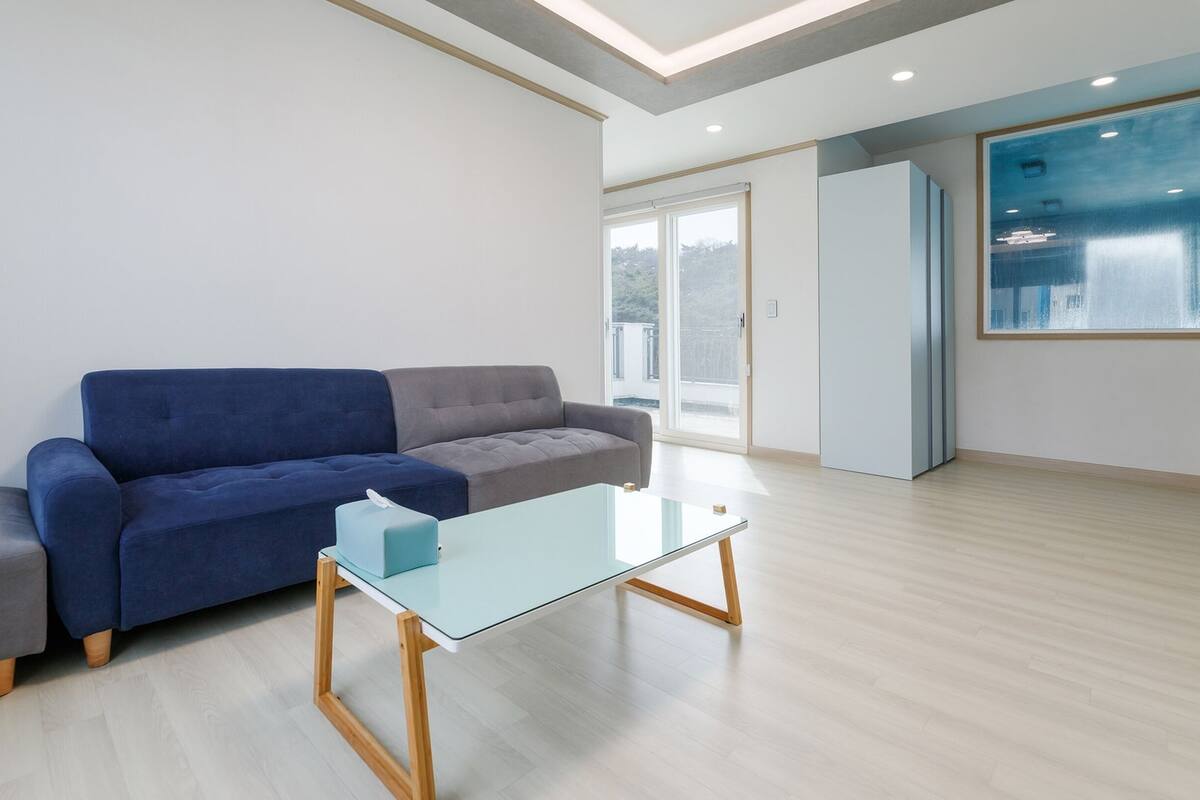 A modern living room with a blue sofa, a glass coffee table, and a large window with a view of the city.