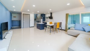 Una sala de estar moderna con un sofá blanco, una mesa de comedor con sillas, una zona de cocina y una escalera que conduce a un piso superior.