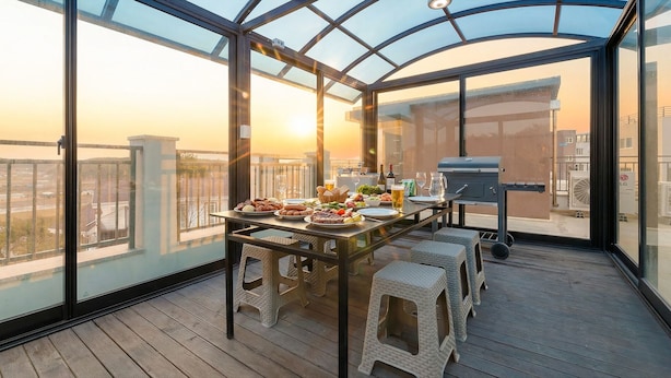 Un área de comedor en la azotea con una mesa dispuesta para una comida, una parrilla y vistas de la ciudad.