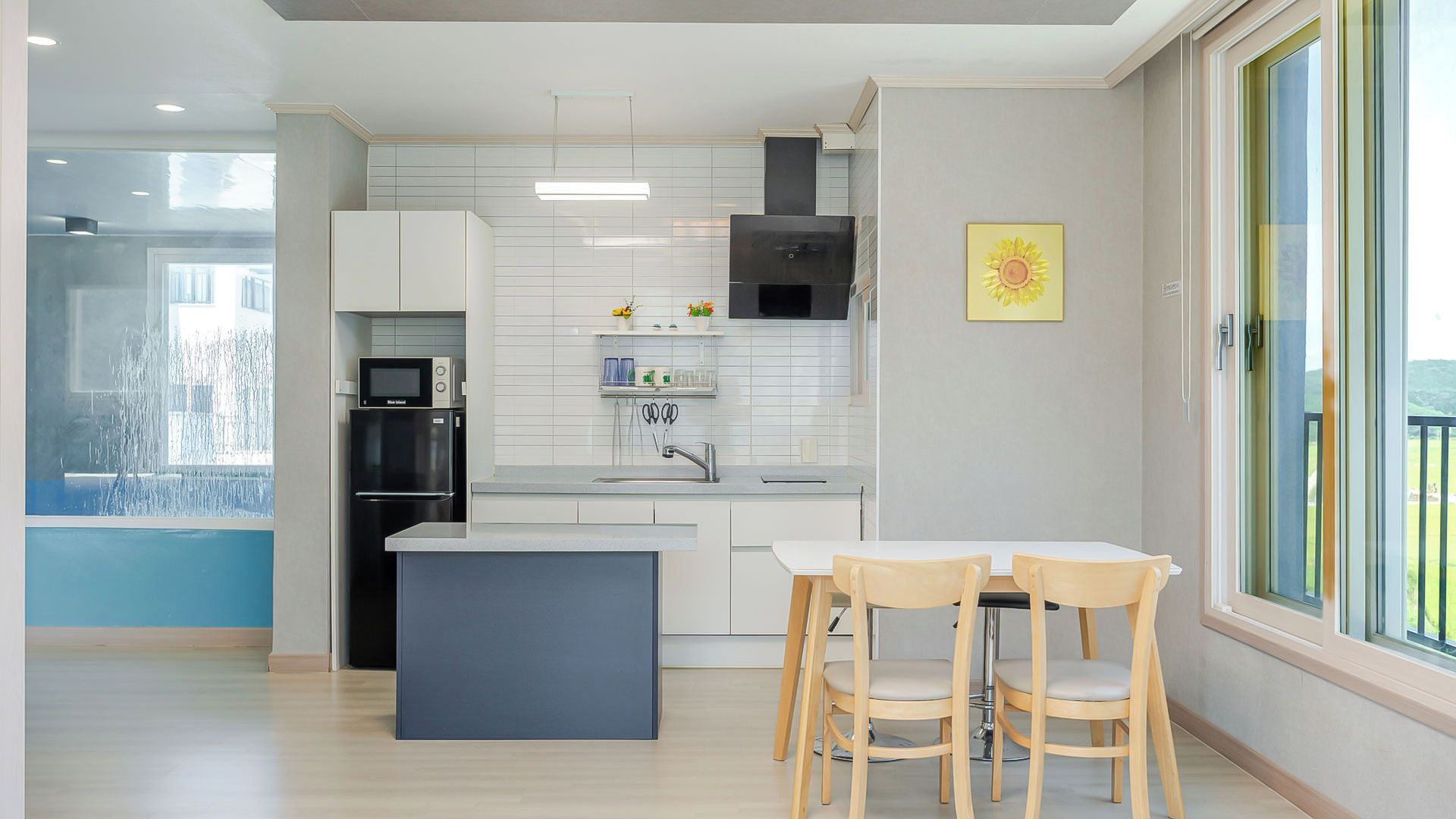 A modern kitchen with white cabinets, a black range hood, and a dining area with two wooden chairs.