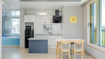 A modern kitchen with white cabinets, a black range hood, and a dining area with two wooden chairs.
