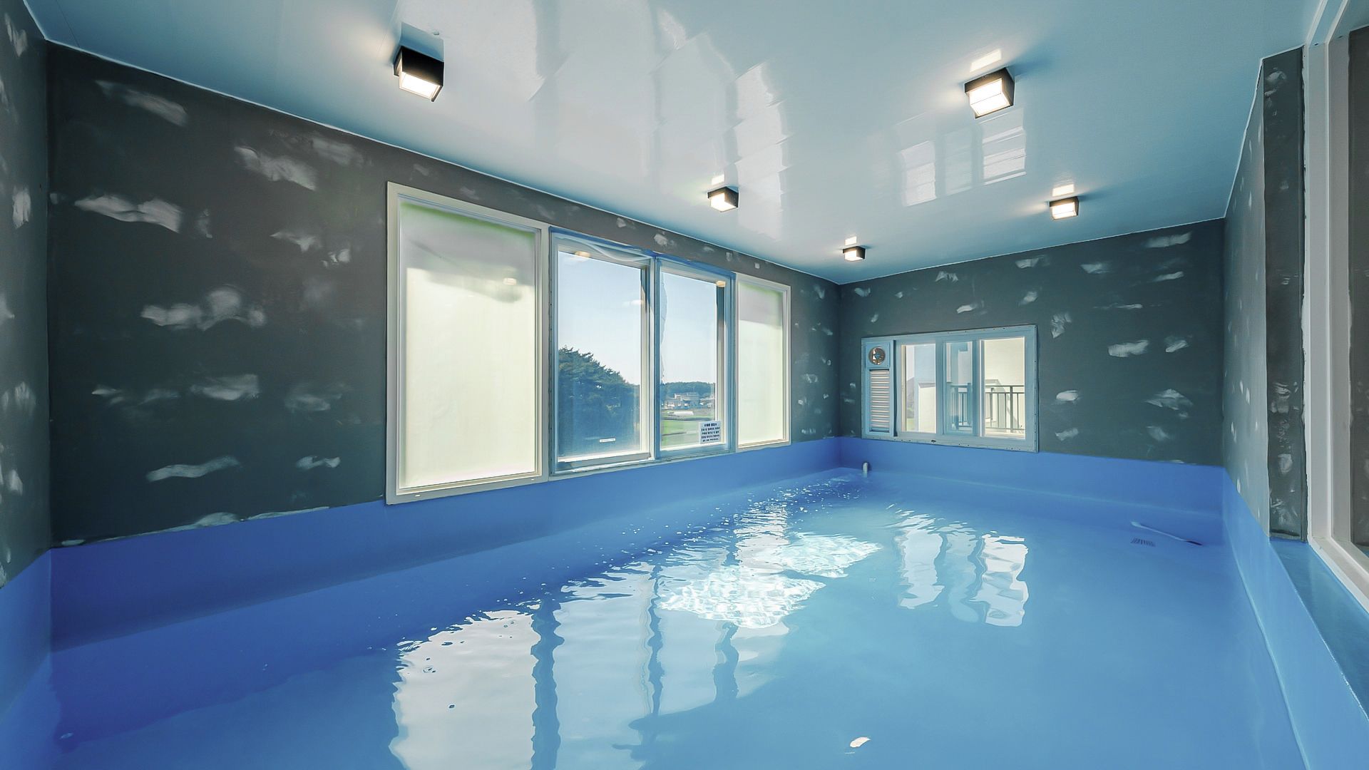 Una habitación con un ventanal grande, una lámpara en el techo y suelo azul.